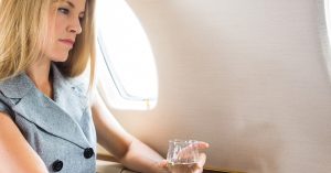 Woman On Private Jet Writes On Laptop, Holding Glass Of Wine
